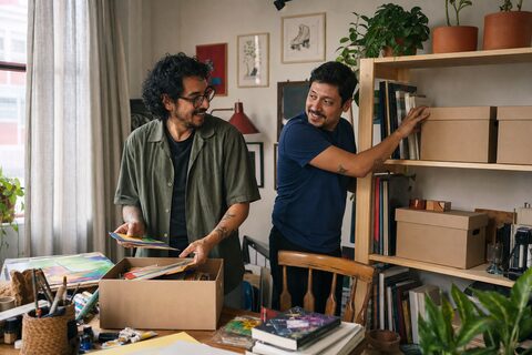 Dos hombres adultos organizan juntos libros y materiales de arte en un apartamento